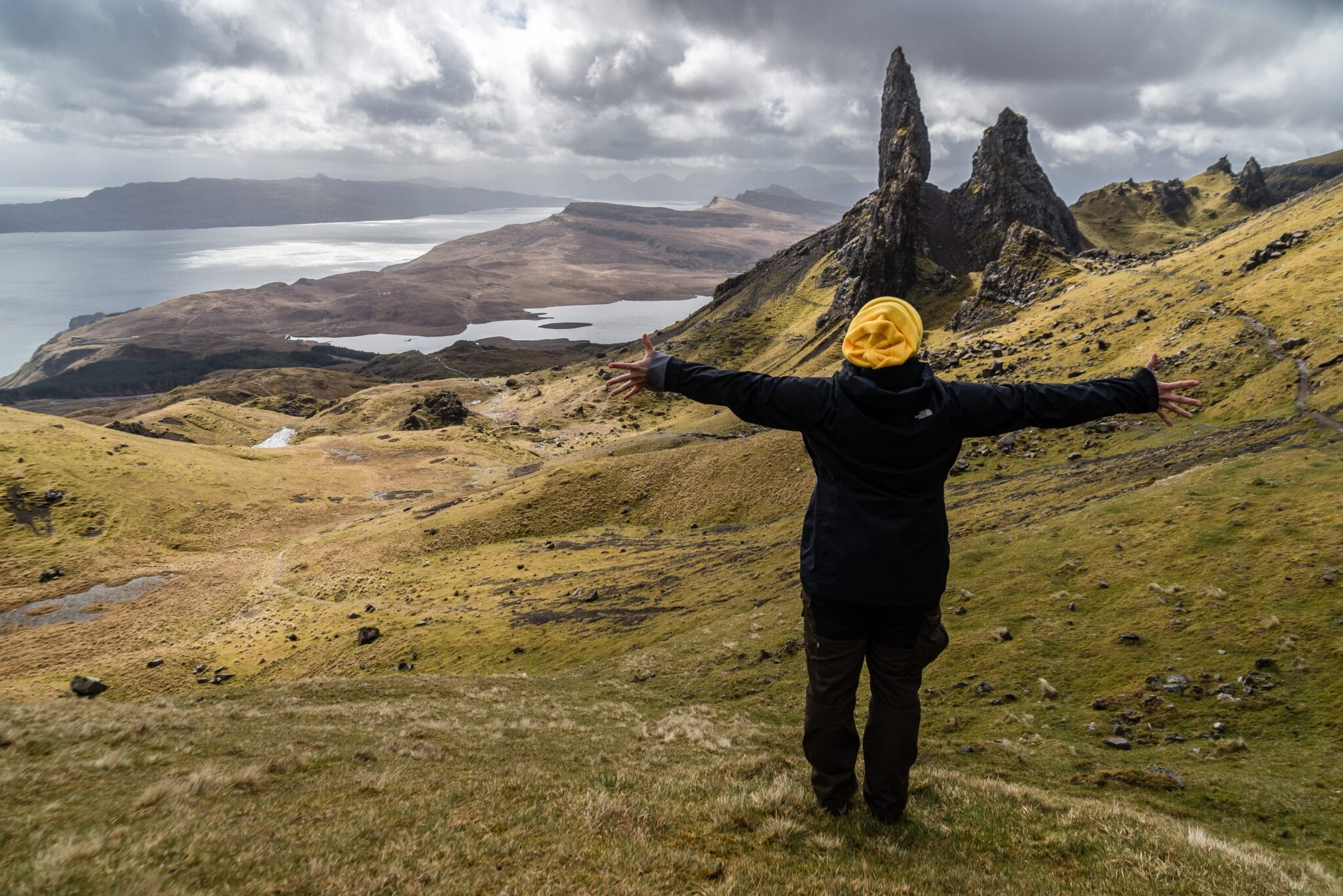 A woam has spread her hands in front of Scottish scenery. Represents and idea of what to do .